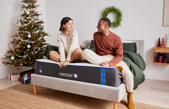 Two people seemingly happy sitting on a Nectar mattress with no sheets